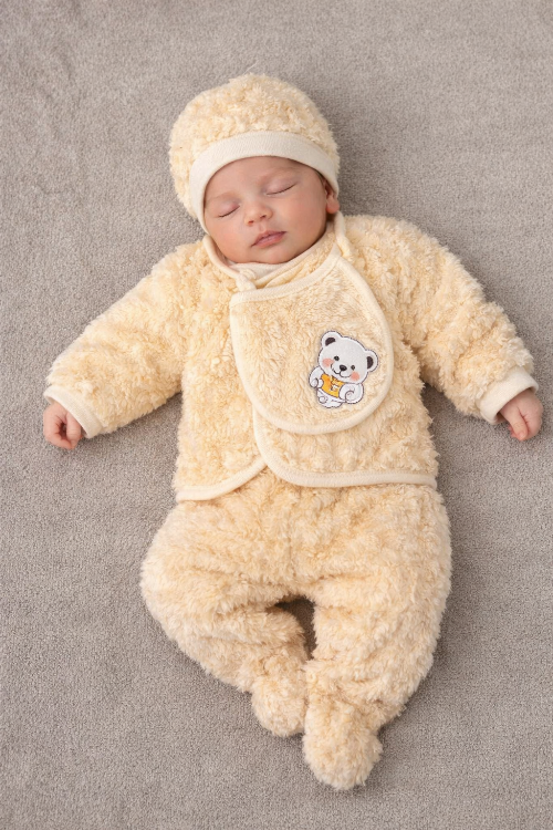 Newborn baby in a cream-colored outfit with a bear design on a gray surface